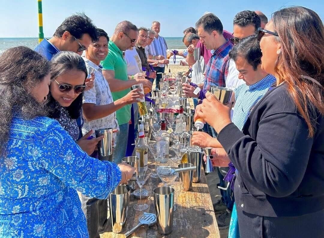 Deelnemers shaken cocktails aan een lange tafel op het strand van Scheveningen